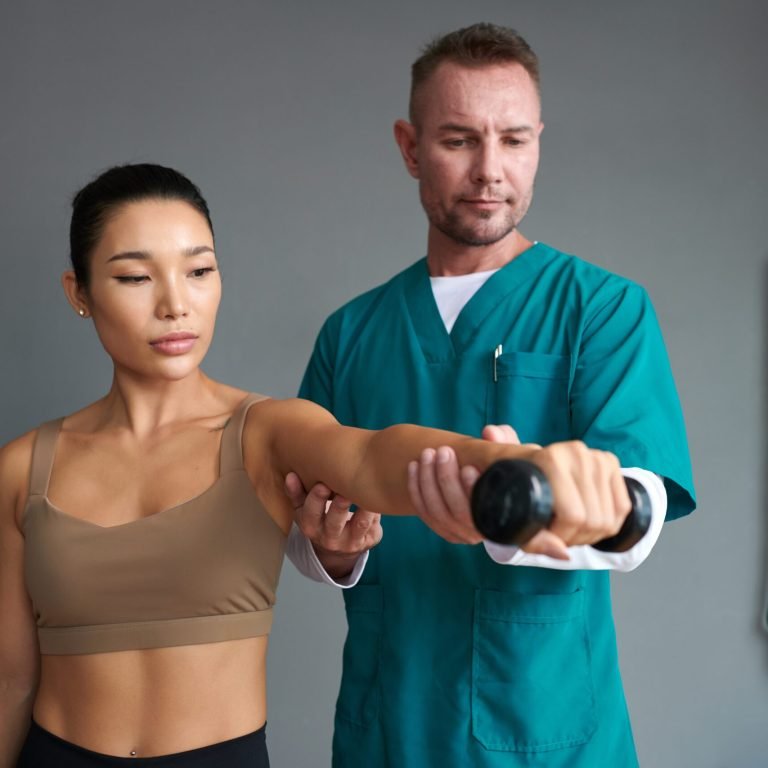 Rehab nurse helping sportswoman to do exercise with dumbbell when recovering from injury